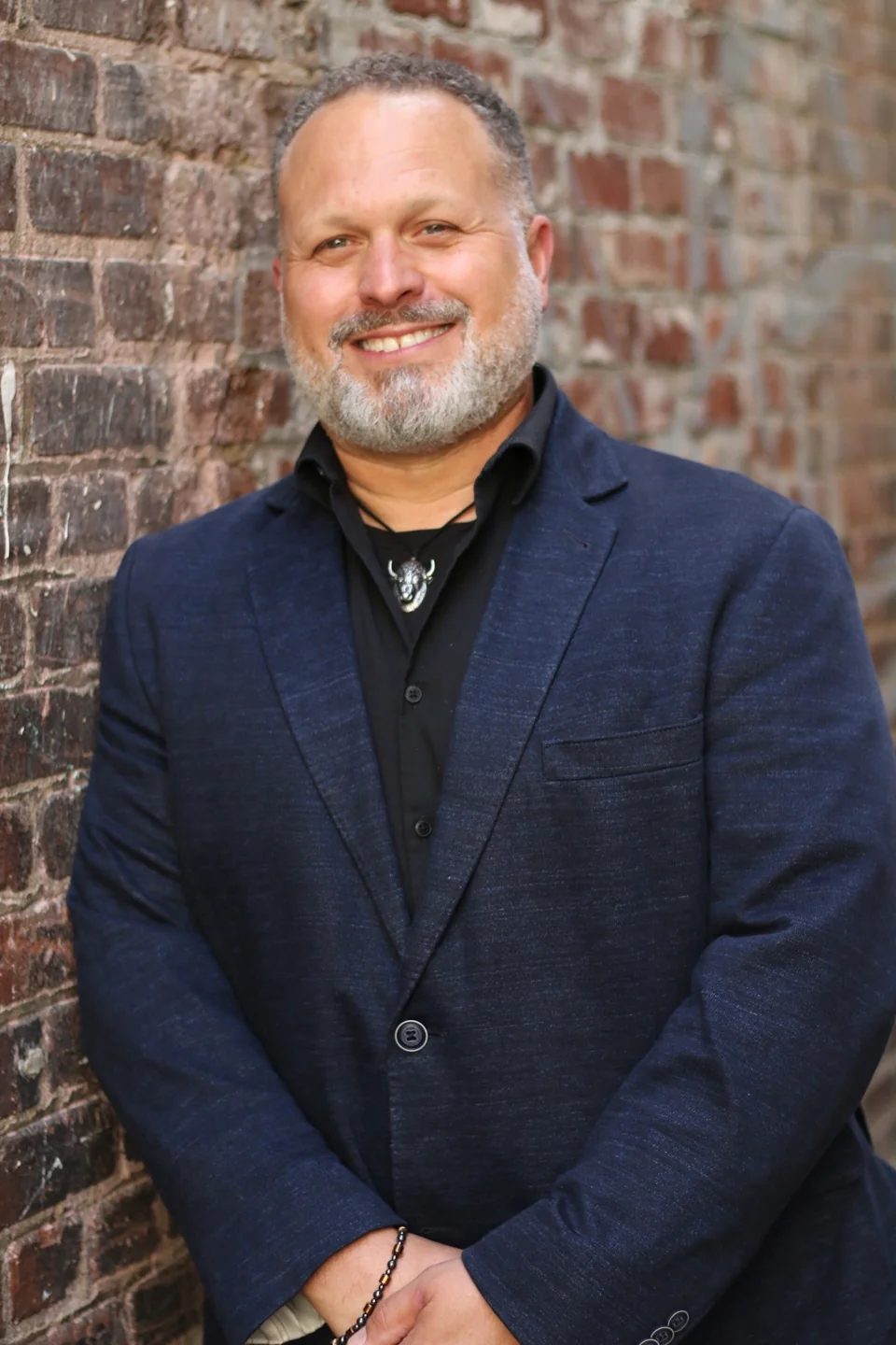 Dennis Landfather smiling beside a brick wall